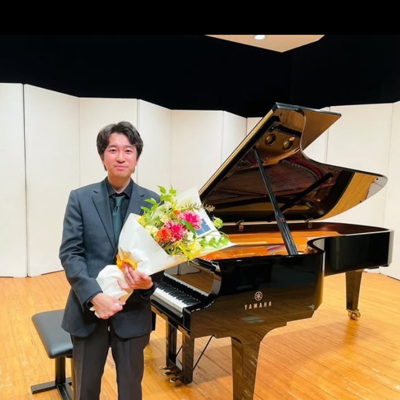 京増修史がピアノの前で花束を持つ画像