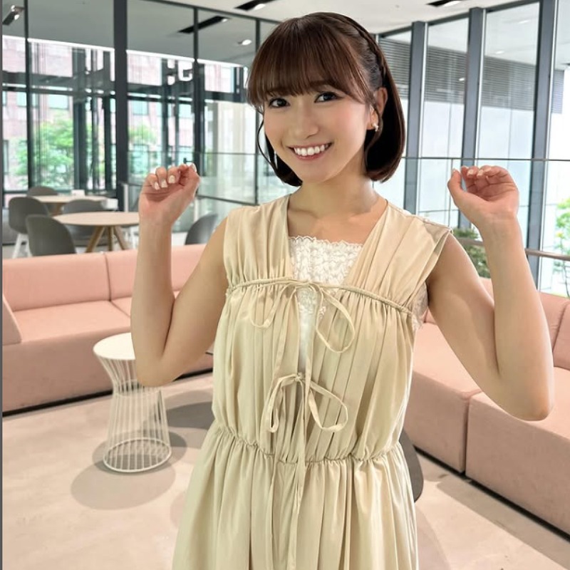 薄茶色の服をきて両手を肘から上にあげる仕草をする廣岡まりあの画像