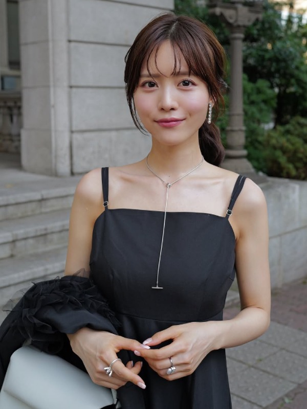 黒いワンピース姿で屋外、重厚なエントランスの前に立つ新田さちかの画像
