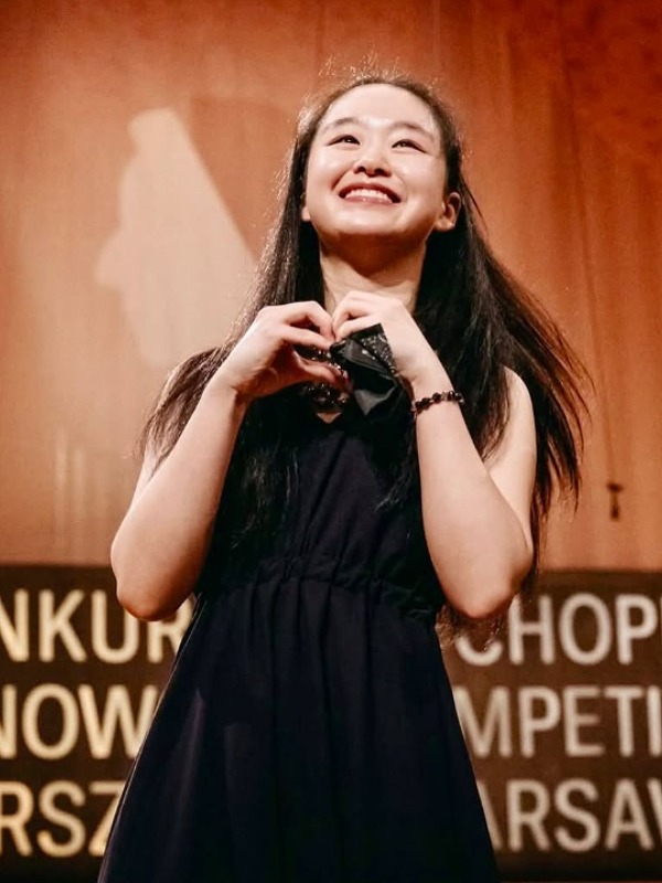 ティエンヤオ・リューがステージ上で黒い服を着て両手でハートマークを作っている画像