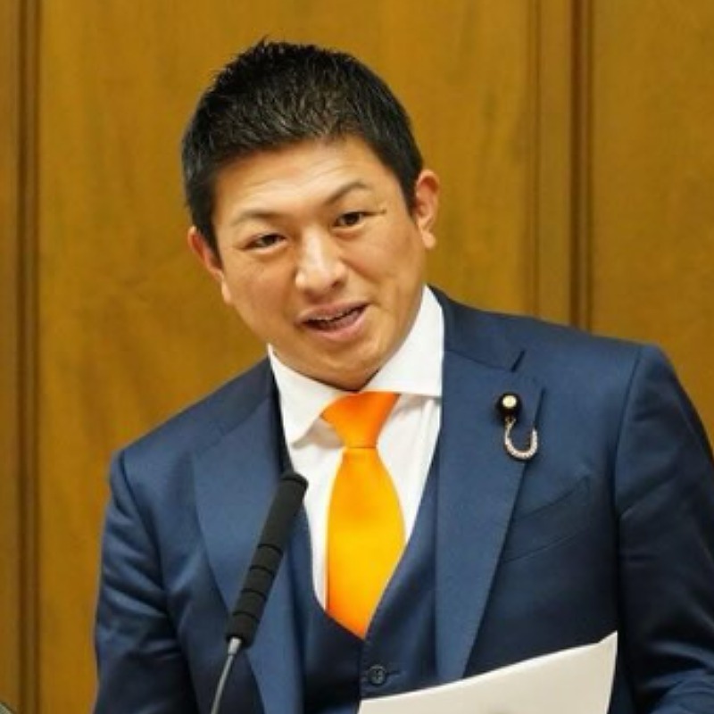 紺色のスーツを着てマイクに向かって話す神谷宗幣の画像