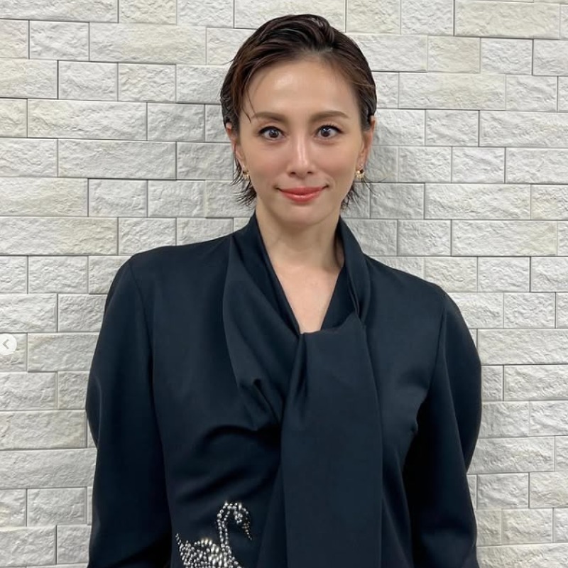 黒い服を着て白いタイル張りの壁の前に立つ米倉涼子の画像