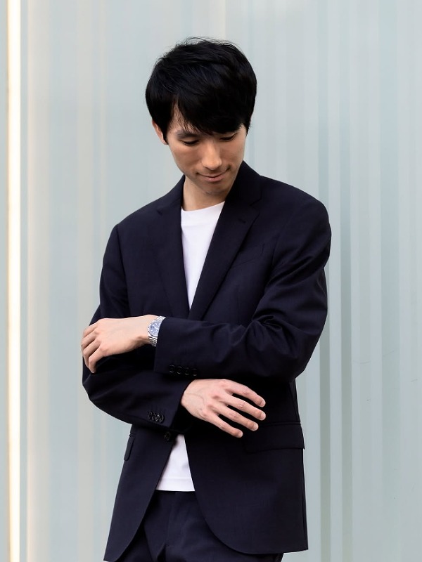 エリック・ルーが黒いジャケットを着て腕を組み下を向いて立っている画像