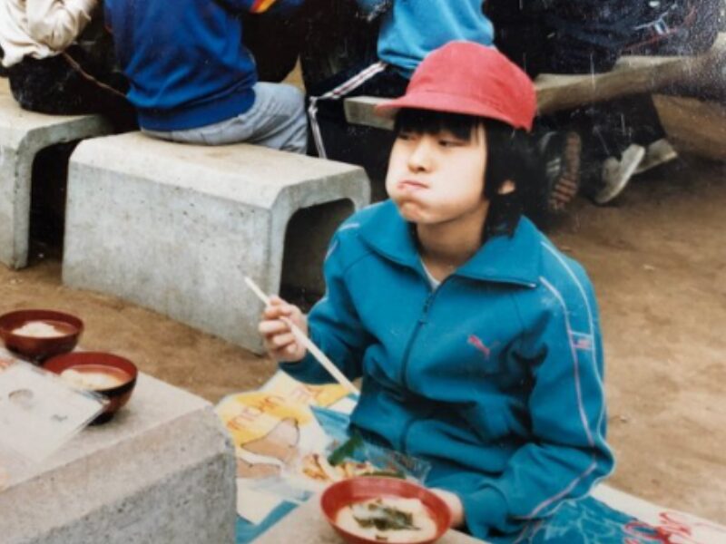 屋外で昼食をほおばる小学生時代のアンジェラ佐藤の画像