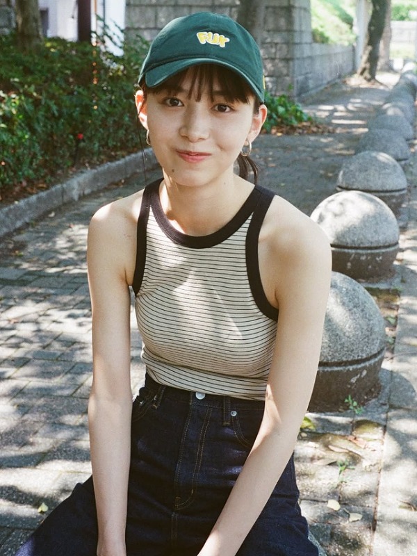 井桁弘恵が緑色のキャップを被り歩道の石の上に座る画像