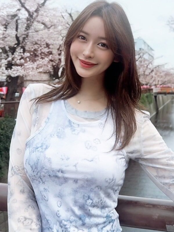 野崎萌香が桜並木の横を流れる川に掛かる橋の上で微笑む画像