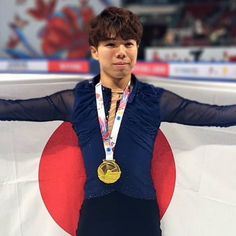 金メダルを首にかけ日の丸を背中に広げる佐藤駿の画像