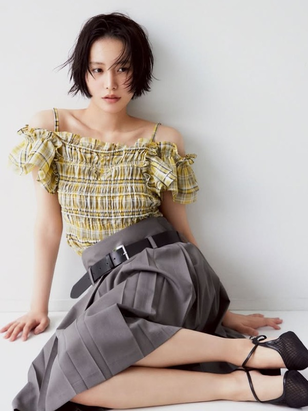 南沙良が黄色のチェック柄服とグレーのすかーを履いて座り壁に寄り掛かる画像