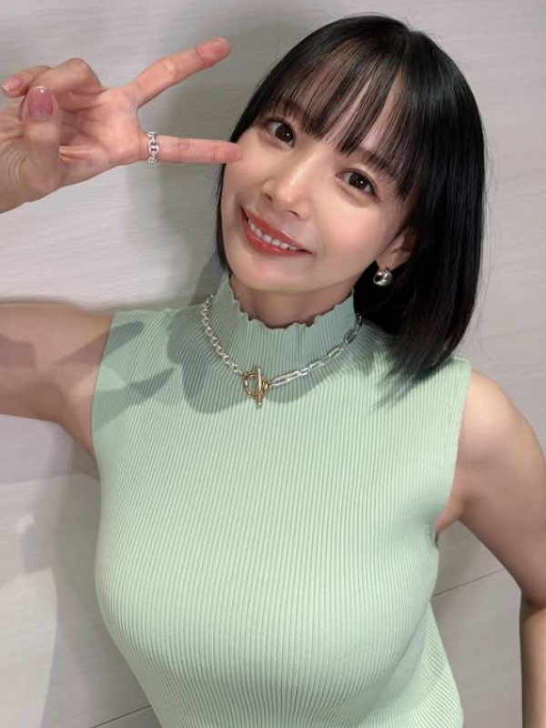 岡田紗佳がメロン色のノースリーブニットを着て右手で目の近くでピースする画像