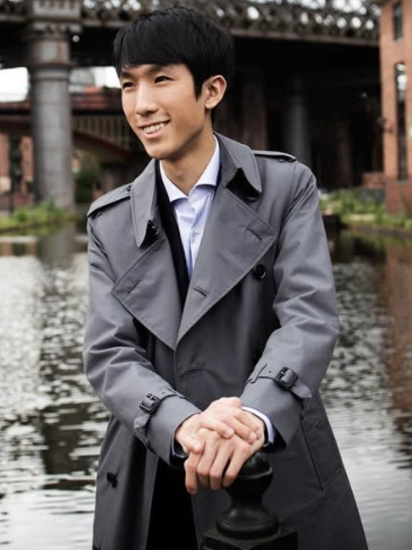 エリック・ルーがグレーのトレンチコートを着て川辺に立つ画像