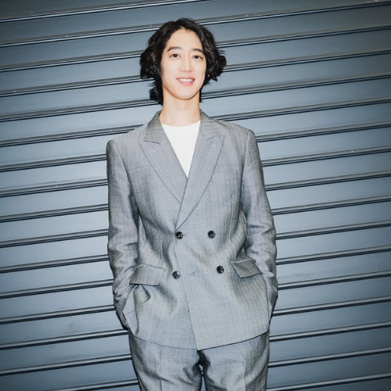 角野隼斗がグレーのスーツ姿でシャッターの前に立つ画像