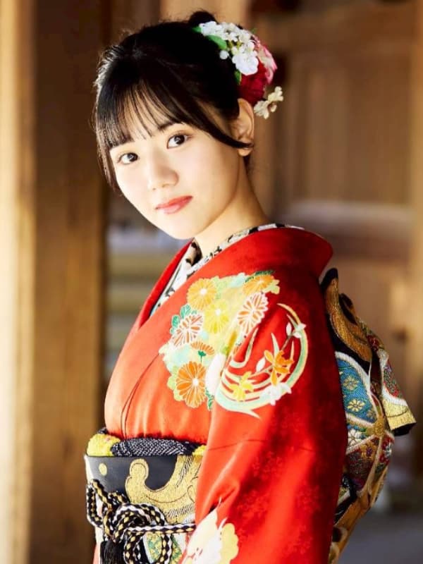 鮮やかな赤地の振袖をまとい、木造建築の前でカメラを見つめる早坂美海。人見知りを克服し、充実した大学生活を送る中で見せる、凛とした芯の強さを感じさせる表情。