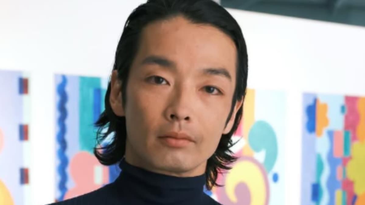 カラフルな抽象画を背景に、濡れたような質感の中長髪で黒のタートルネックを着た、真剣な表情の森山未來のポートレート。