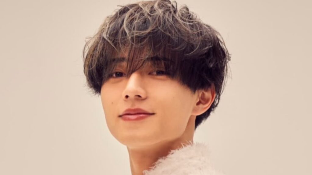 眉上の重めのアッシュグレーヘアで、白いフワフワした上着を着て微笑む永瀬廉のバストアップ写真。