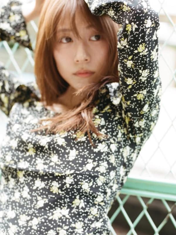 黒地に白い花柄が描かれたワンピースを着用し、屋外のフェンスを背にリラックスした表情を見せる有村架純。自然光に包まれたアンニュイな雰囲気のポートレート。