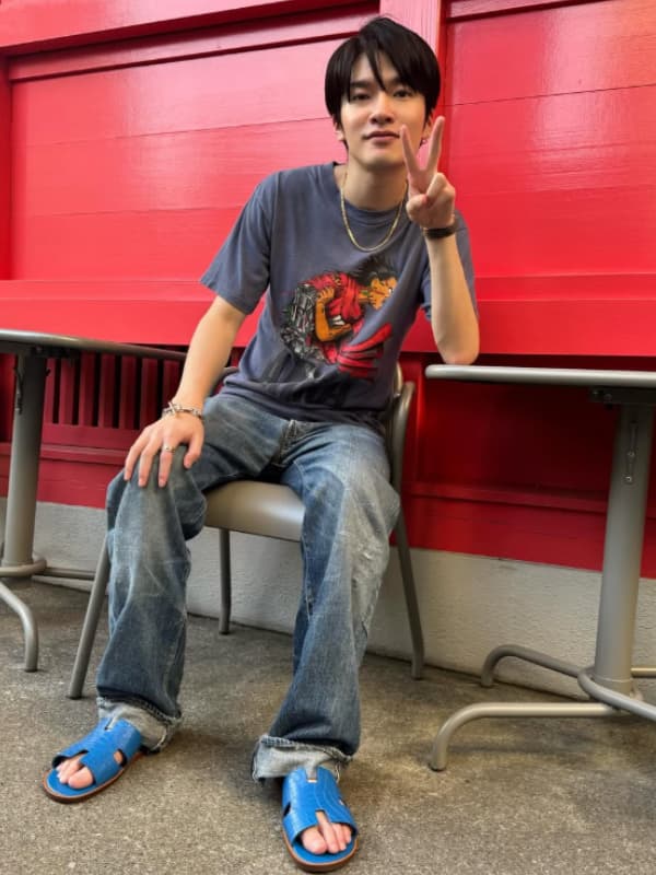 深澤辰哉が神社の社の脇で椅子に座りピースサインをする画像