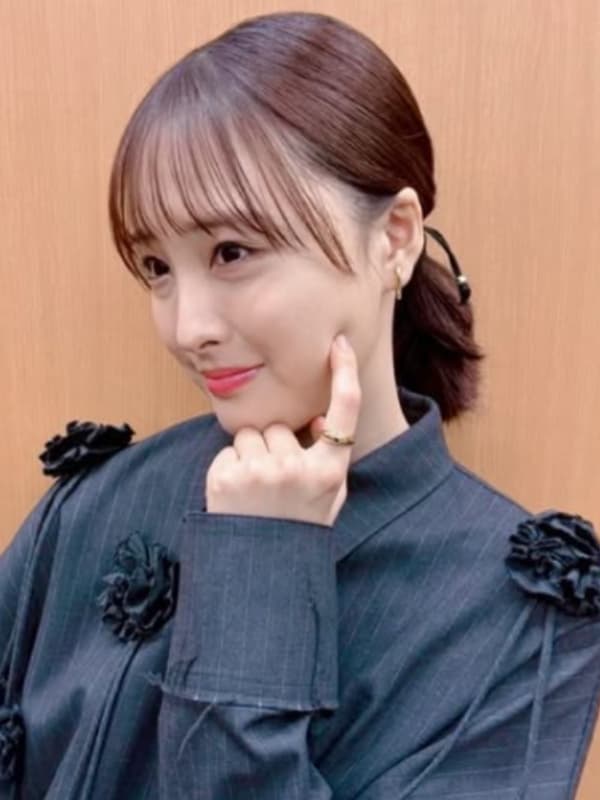 肩に花のモチーフがあしらわれた濃紺のワンピース姿で、人差し指を頬に当てて茶目っ気たっぷりにポーズをとる大友花恋。