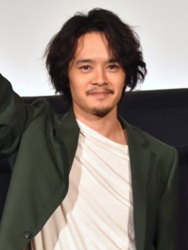 池松壮亮がステージ上で黒いジャケットを着て右手を大きく上げる画像