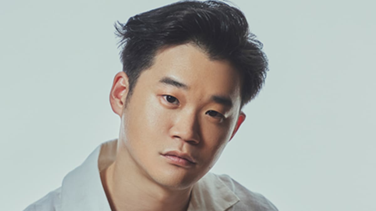 矢本悠馬氏のクローズアップポートレート。白シャツを着用し、カメラを見つめている。