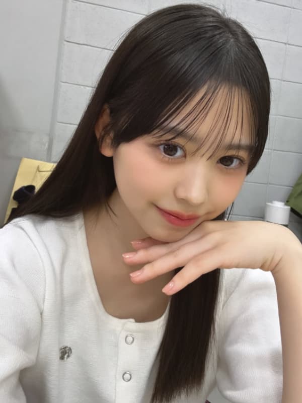 白いカーディガンを着用し手を顎に添えて微笑む梶原叶渚のナチュラルな自撮り写真