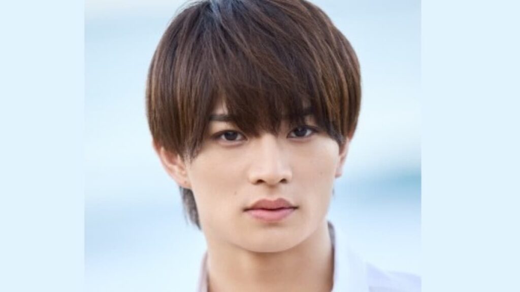 茶髪で落ち着いた表情を浮かべる浮所飛貴のクローズアップ写真。背景は淡いブルーで、清潔感のある白いトップスを着用している様子。