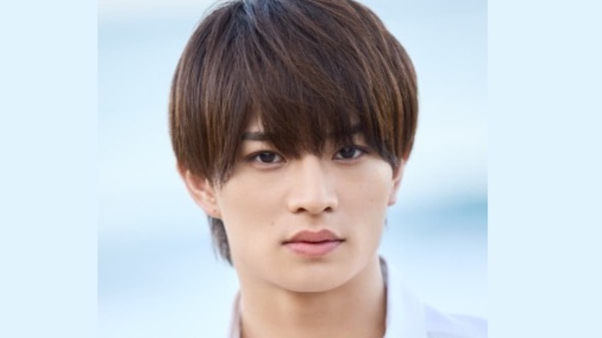 茶髪で落ち着いた表情を浮かべる浮所飛貴のクローズアップ写真。背景は淡いブルーで、清潔感のある白いトップスを着用している様子。