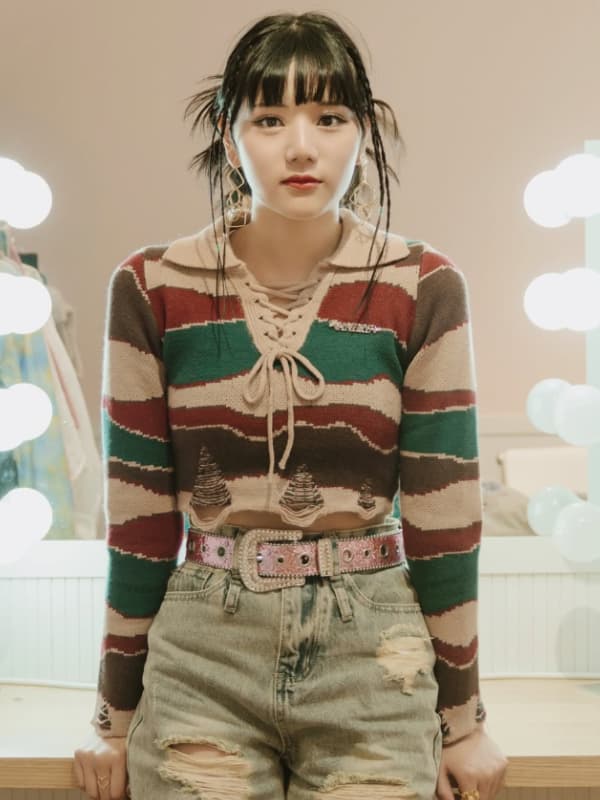 マルチカラーのクロップドニットとダメージジーンズを着用し、楽屋の鏡の前でポーズをとる早坂美海。雪印メグミルク『さけるチーズ』CMでの受験生役とは一味違う、トレンドを意識したファッショナブルな姿。
