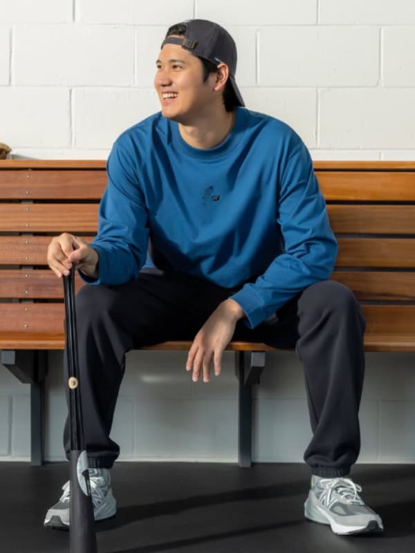 大谷翔平が青い服を着てベンチに座りバットを持つ画像