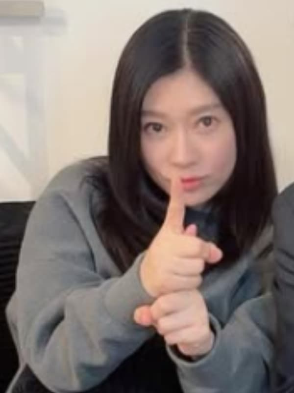 グレーのスウェットを着たカジュアルな姿で、人差し指を口元に当てて「内緒」のポーズをする篠原涼子。