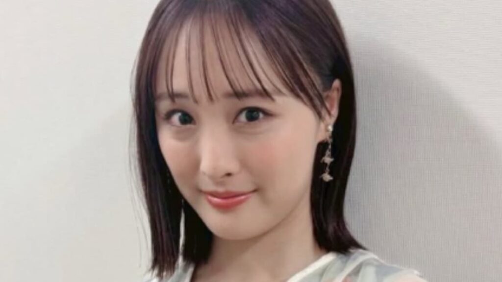 前髪を切り揃えたストレートヘアの大友花恋が、白い花柄のトップスと揺れるイヤリングを身に着けて微笑むポートレート。