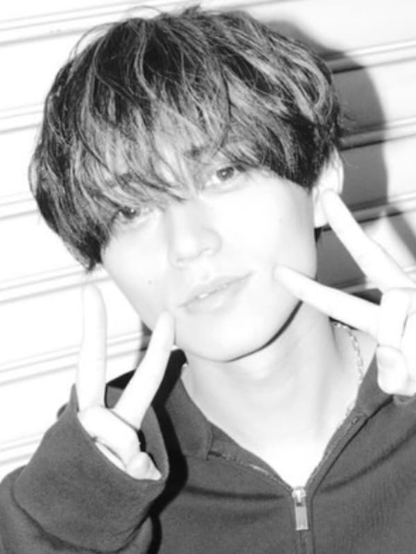 モノクロ画像で、黒いパーカーを着て両手でピースサインをする、眉上のマッシュヘアの永瀬廉。