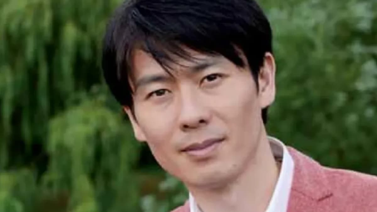 緑豊かな公園を背景に、ジャケットを着用した福間洸太朗のポートレート。