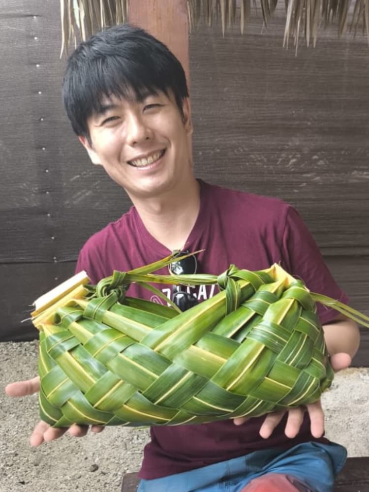 ビーチで、編んだ椰子の葉のバッグを手にする福間洸太朗。