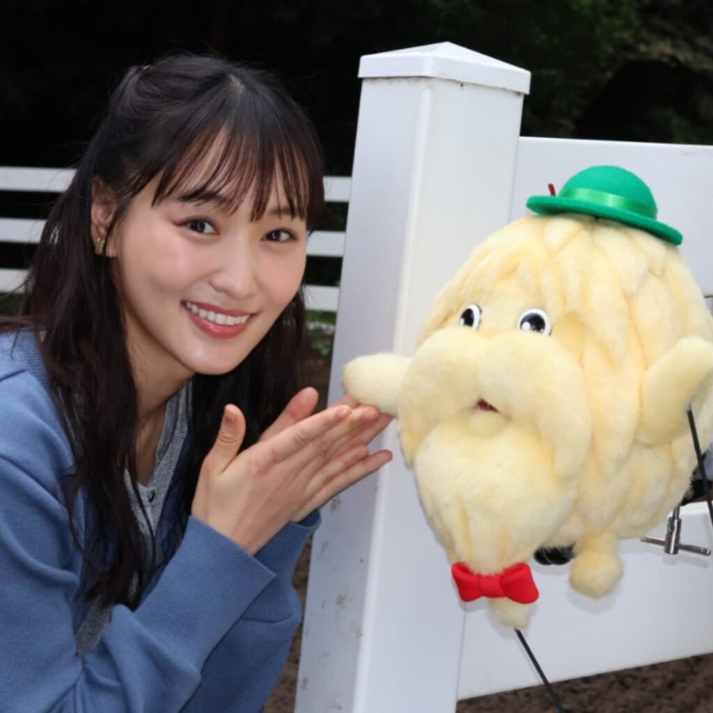 青いケーブルニットセーターを着用した菅井友香が、NHKの番組『ダーウィンが来た！』のキャラクターである黄色いモフモフした体と立派な白ヒゲ、緑の帽子、赤い蝶ネクタイが特徴の「ヒゲじい」の隣で、楽しそうに顔を寄せて微笑んでいるツーショット写真。