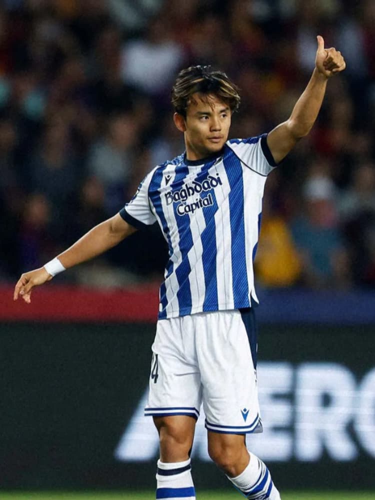 レアル・ソシエダのユニフォームを着用し、左手の親指を立ててサムズアップのポーズをとる久保建英のクローズアップ。