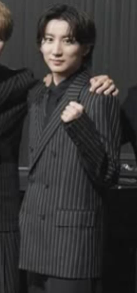 グレーに白いストライプのスーツと黒いインナーを着用した京本大我が、グレーのカーテンを背景に、右手を握ってガッツポーズをしている。