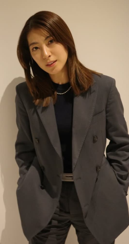 カメラを見て微笑む瀧本美織氏。グレーのスーツを着用。