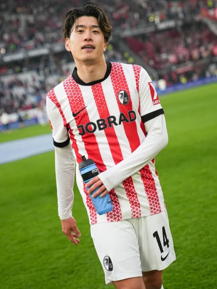 試合後または練習の合間に、青いウォーターボトルを手に持ちリラックスした表情を浮かべるSCフライブルクの鈴木唯人選手。