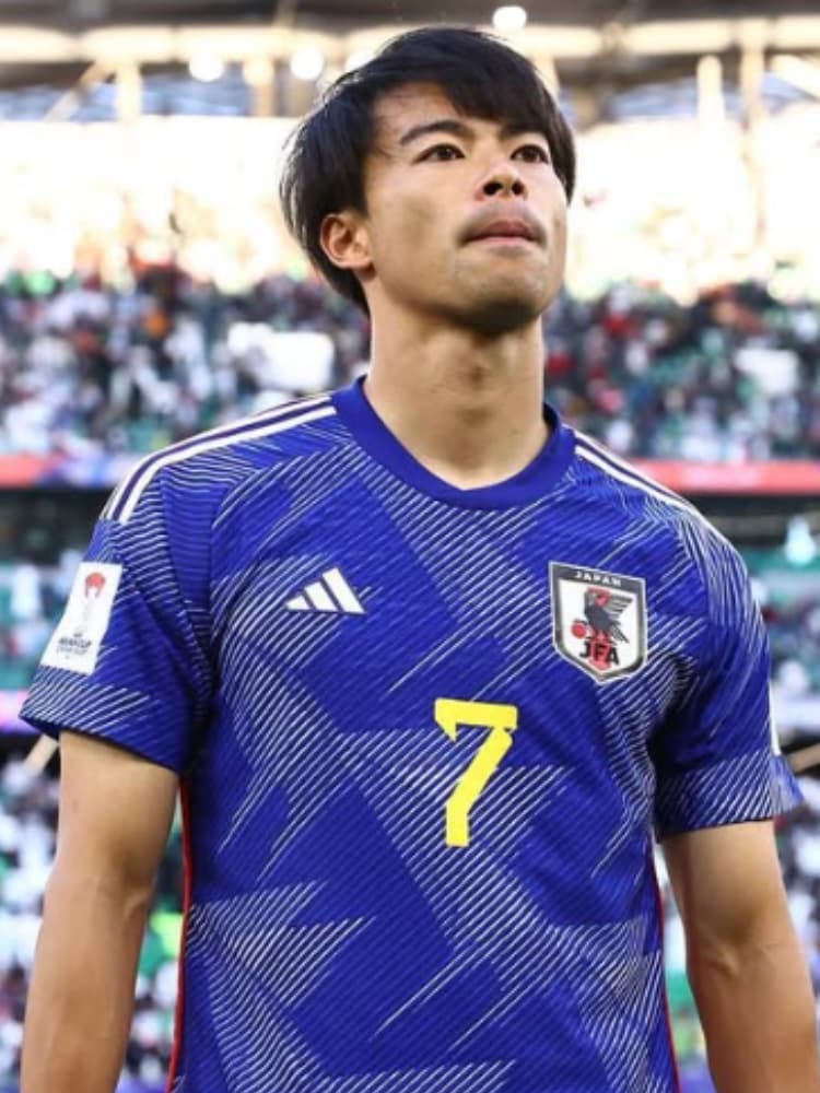 サッカー日本代表の青いユニフォーム（背番号7）を着用し、試合後のピッチで感極まるような表情の三笘薫選手。