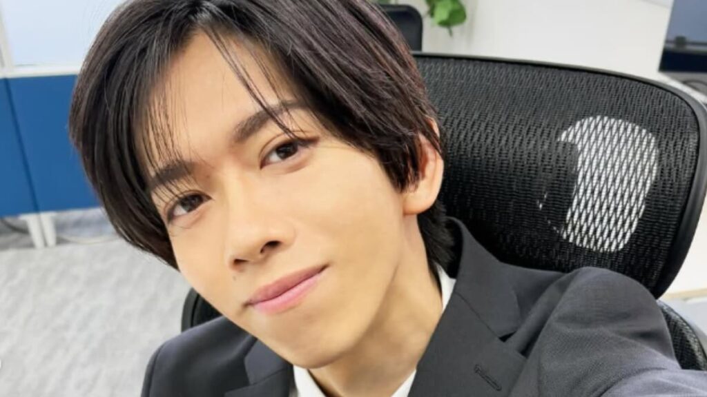 オフィスのデスクチェアに座り、カメラを見つめて穏やかな笑みを浮かべる船津稜雅。黒いスーツと白いシャツを着用。