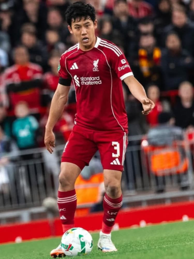 リヴァプールFCの赤いホームユニフォームを着用し、アンフィールドのピッチでボールを足元に置き、前方を見据えてプレーする遠藤航選手。