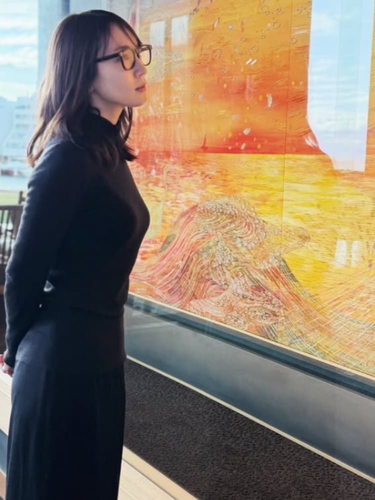 黒タートルネックとメガネ姿で、巨大な絵画を熱心に鑑賞する吉岡里帆の横顔写真。