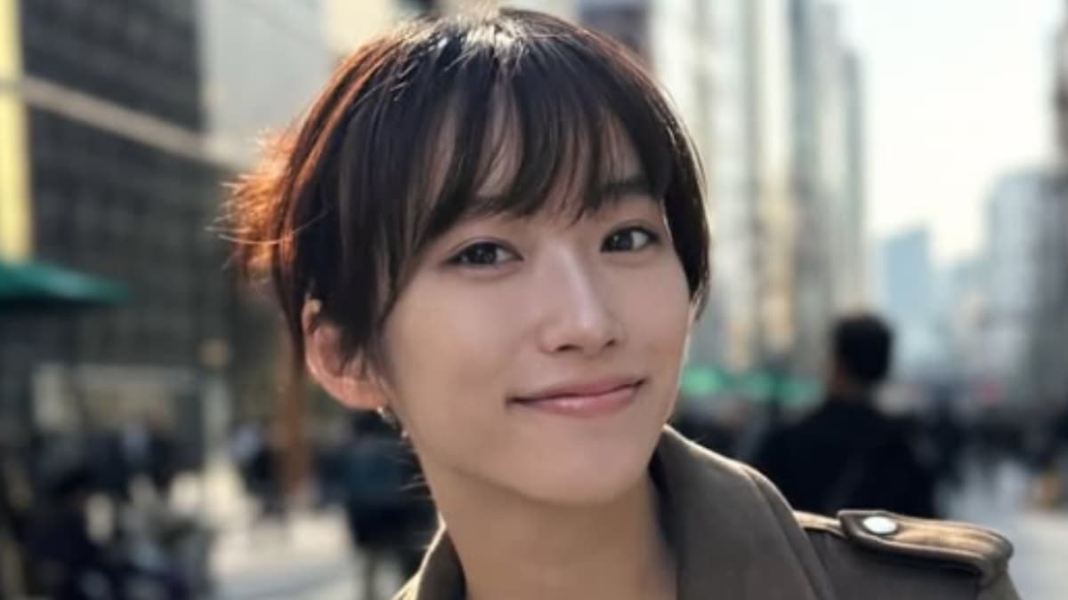 街角で微笑む、茶色のショートヘアの片岡凜。茶色のレザージャケットを羽織り、背景はぼやけたビル群。