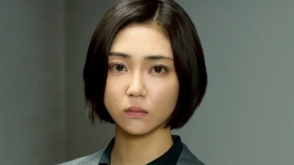 暗いショートボブヘアで真剣な表情をした山谷花純の正面アップ写真。グレーのジャケットと黒いトップを着用している。背景はぼやけたグレー。