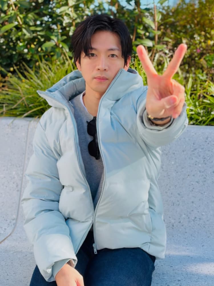 大河ドラマ 『豊臣兄弟！』 や 『銀河の一票』 など、2026年の過密スケジュールの合間に、屋外のベンチでリラックスした表情を見せる松下洸平。淡いブルーのダウンジャケット姿で、ファンへの親しみやすさを感じさせるピースサインをする。