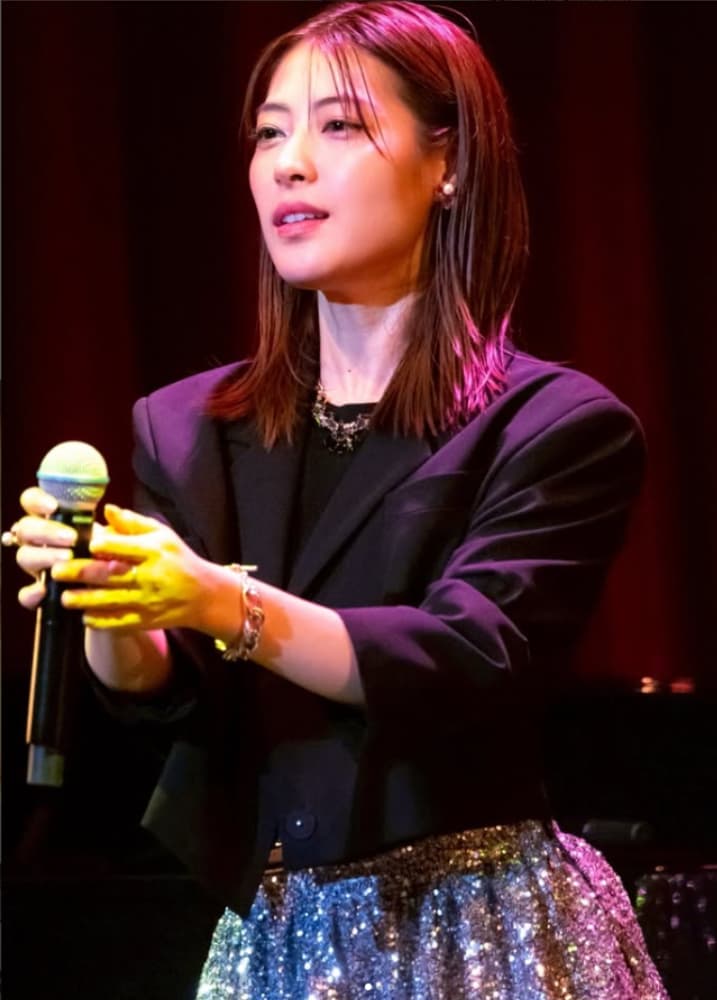カメラを見て歌う瀧本美織氏。黒いスーツを着用。
