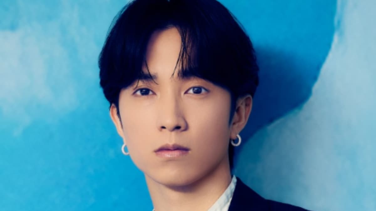 黒髪のクローズアップショット。田中樹は黒いジャケットに白い襟のシャツを着用し、ゴールドのフープイヤリングをつけている。真剣な表情でカメラを直接見つめている。背景は青い水彩風のテクスチャ壁。