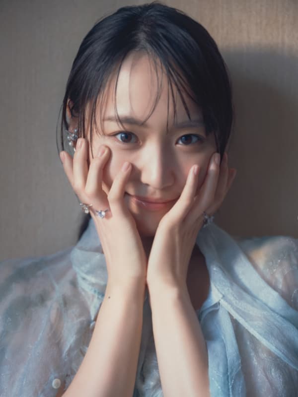 淡い水色のシアーなブラウスを身につけ、両手を頬に添えてまっすぐカメラを見つめる菅井友香のクローズアップ。指先には繊細なリングが光る。
