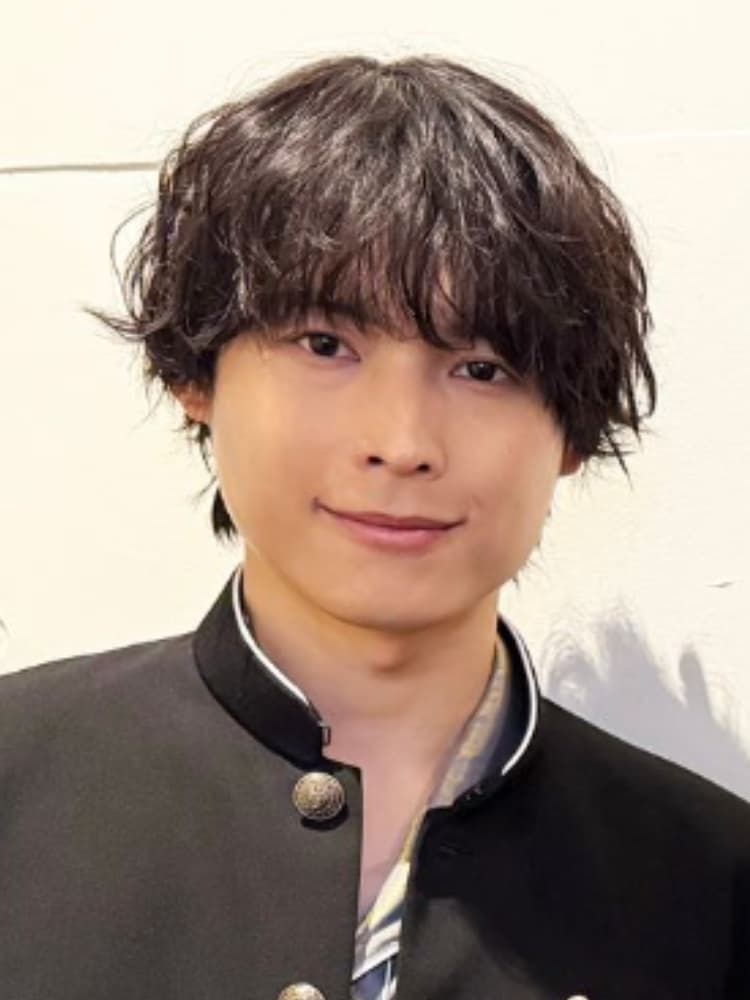 松村北斗氏。黒い髪がラフにスタイリングされており、少し微笑んでいます。リラックスした表情です。黒い学生服（学ラン）を着用。襟にはボタンがあり、白いラインが2本入っています。