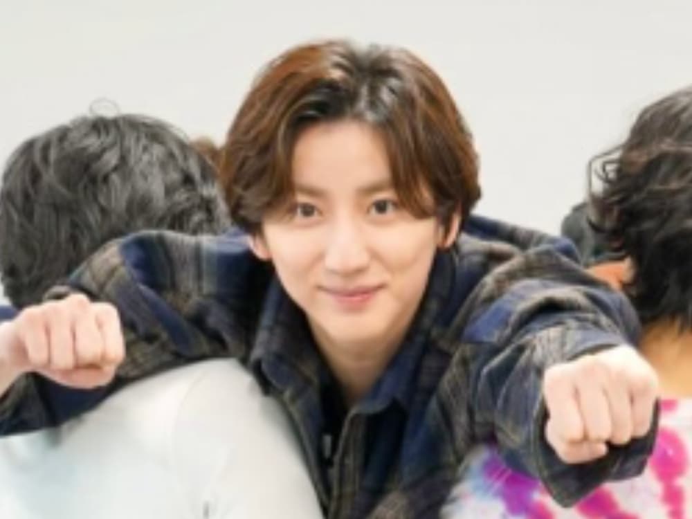 グレーのパーカーとカラフルなストライプのTシャツを着用した京本大我が、白い背景で他の人に肩を組まれ、笑顔でカメラを見ている。